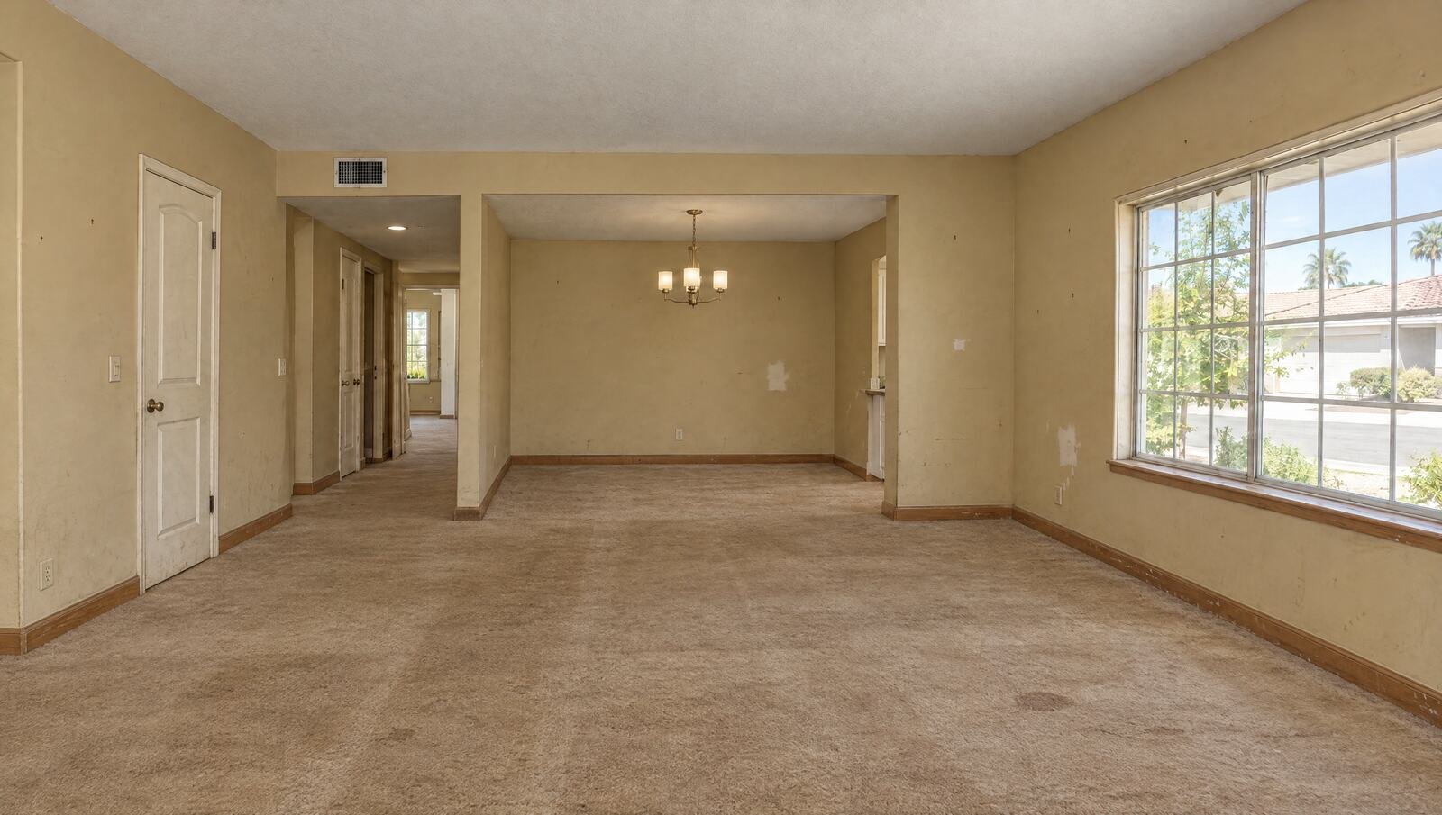 The same room before: worn tan carpet, scuffed yellow-beige walls with patch marks, stained oak baseboards